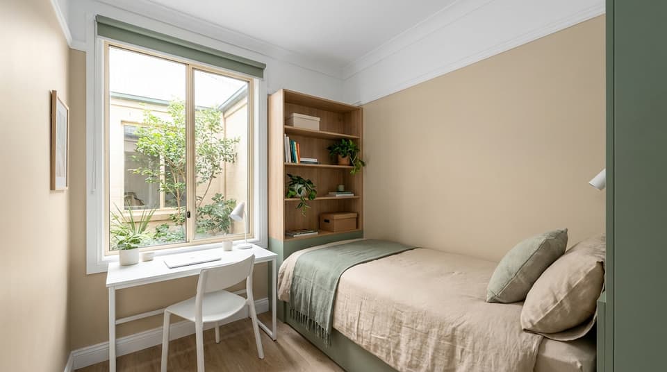 Compact solo room with single bed, slim desk, and a courtyard-side window.