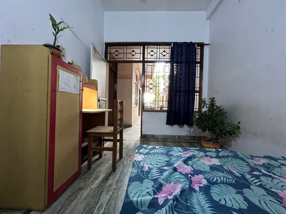 Spacious furnished room with a bed, desk, storage, and a large window.