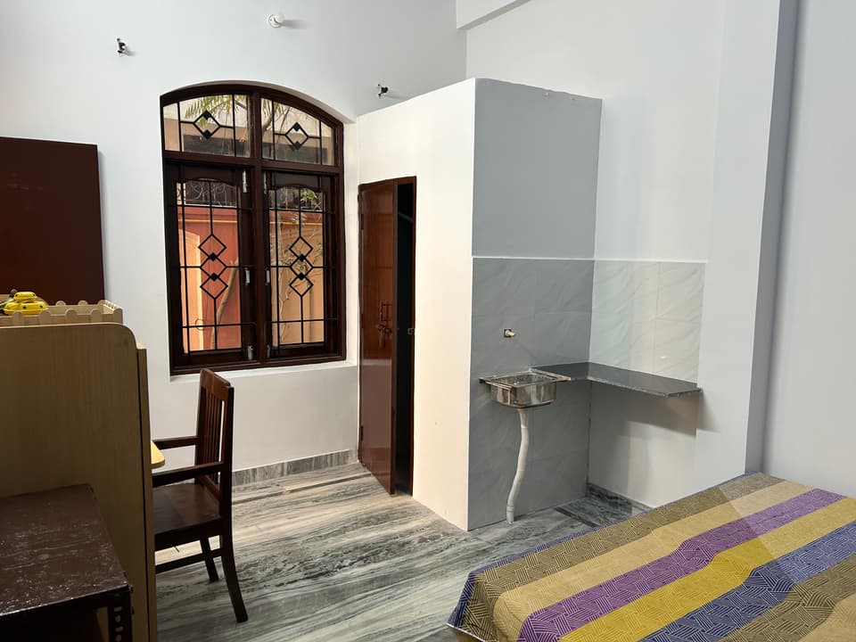 Bed, private kitchen counter, and washroom door inside the studio.